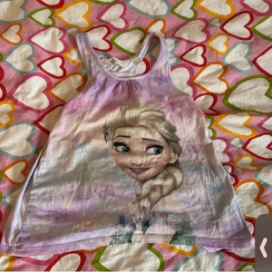 Linnetopp med motiv - Söt linnetopp med motiv av en känd karaktär. Toppen har en mjuk färgskala i lila och rosa toner. Perfekt för varma sommardagar.