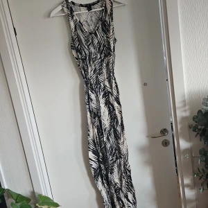 Mönstrad ärmlös klänning - Snygg ärmlös klänning med svartvitt mönster och knytband i midjan. Perfekt för en somrig look med sin lätta och luftiga design. Klänningen har en v-ringad hals och är i en lång modell.