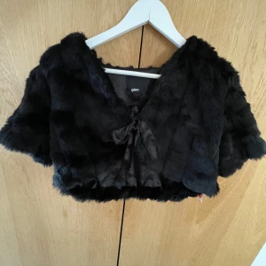 Svart pälsbolero  - Säljer en snygg svart pälsbolero från Gina med korta ärmar och knytband framtill. Jackan är croppad och perfekt för att ge en lyxig touch till din outfit. Den har en mjuk och fluffig känsla som gör den både stilren och bekväm.Priset går att diskutera!❤️