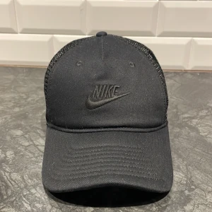Svart keps från Nike - Snygg svart keps från Nike med meshdetaljer på baksidan för extra ventilation. Justerbar passform med spänne bak. Perfekt för en sportig look eller vardagsstil. Nypris 350kr 