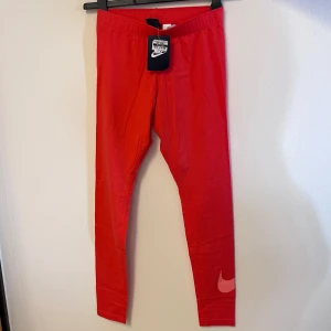 Neon Röda leggings från Nike - Snygga röda leggings från Nike med en ikonisk logga på benet. Perfekta för träning eller en sportig look. Tillverkade i ett stretchigt material för bästa komfort.