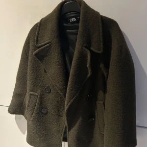 Olivgrön kappa från Zara - Säljer en stilren olivgrön kappa från Zara. Den har en klassisk dubbelknäppt design med stora knappar och breda slag. Perfekt för höst och vinter. 🧥 medium lång i längden