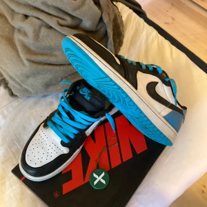 Nike Air Jordans med blå detaljer - Säljer ett par Nike Air Jordans med en stilren design i svart, vit och blå. Skorna har blå snörning och en iögonfallande blå sula. Perfekta för dig som vill ha en sportig och trendig look.