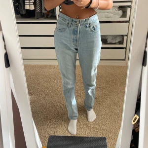 Ljusblå jeans Levis 501 - Snygga ljusblå jeans som är mid waist. Står att de ska vara korta ner till men är hela vägen till fötterna på mig som är 169 cm! Använda max 10 gånger, så är i bra skick. Storlek 24 i midjan och 30 i längd