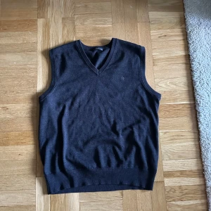 Svart stickad väst från Manstar Roma - Säljer en stilren svart stickad väst från Manstar Roma. Västen har en klassisk v-ringad design och är perfekt för lager-på-lager. Den är mjuk och bekväm, idealisk för både vardag och mer uppklädda tillfällen. Finns två stycken små hål i denna tröja tyvärr..