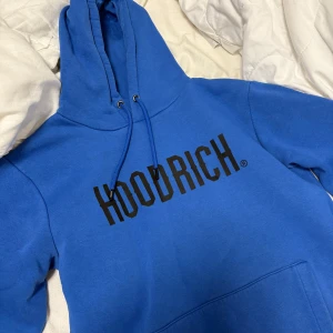 Blå hoodie från Hoodrich - Säljer en snygg blå hoodie från Hoodrich med svart text på bröstet. Den har en klassisk design med dragsko i huvan och en stor magficka. Perfekt för en avslappnad stil. 🌀