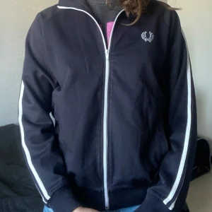 Kofta från Fred Perry - Cool kofta från Fred Perry med dom klassiska revären på armarna. Skulle säga att den är ish marinblå men nästan svart. Använd men i bra skick!