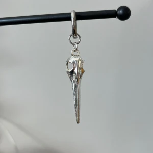 Silverfärgat örhänge i rostfritt stål med fågelkraniumdesign - Unikt örhänge i silverfärg med en design som liknar ett fågelkranium. Detaljerad och stilren, perfekt för att ge en edgy touch till din stil.