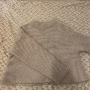Beige stickad tröja - Säljer en mysig beige stickad tröja med ribbad struktur. Tröjan har en hög hals och långa ärmar, perfekt för kyliga dagar. Den är både stilren och bekväm, ett måste i garderoben!