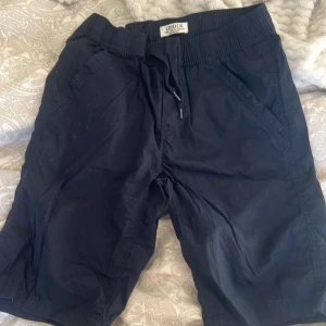Mörkblå shorts från Lindex barn  - Snygga mörkblå shorts från Lindex med elastisk midja och snörning för extra komfort. Perfekta för en avslappnad stil. De har två sidofickor och är gjorda i ett lätt och bekvämt material.