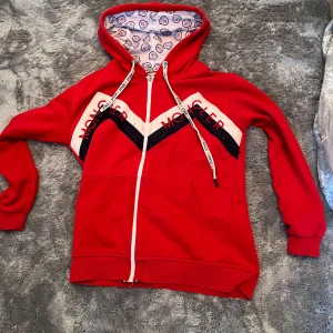 Röd hoodie från Moncler - Snygg röd hoodie från Moncler med dragkedja och mönstrad insida i huvan. Tröjan har långa ärmar och Moncler-logga på bröstet. Perfekt för en avslappnad stil. 