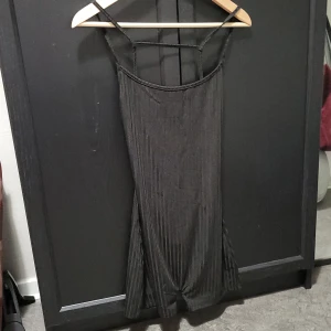 Svart klänning med smala axelband - Svart jumpsuit med smala axelband och plisserad design.