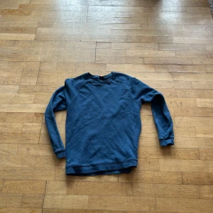 Blå sweatshirt - Säljer en stilren blå sweatshirt med långa ärmar. Perfekt för en avslappnad look. Tröjan har en klassisk design med ribbade muddar vid ärmslut och nederkant. skriv om ni undrar något