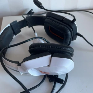 Gamingheadset med mikrofon - Säljer ett gamingheadset i svart och vitt med inbyggd mikrofon. Headsetet har vadderade öronkuddar för extra komfort och ansluts via USB. Perfekt för långa spelsessioner.