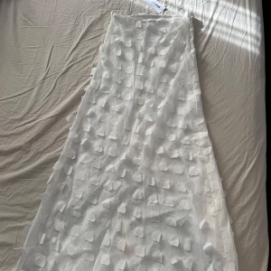 Vit långkjol med 3D-detaljer - Säljer en elegant vit långkjol med unika 3D-detaljer som ger en lyxig känsla. Kjolen har en dragkedja i sidan för enkel på- och avtagning. Finns matchande topp💕