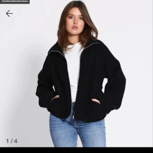 Svart teddyjacka med dragkedja från lager 175 - Mysig svart teddyjacka med dragkedja framtill. Perfekt för kyliga dagar och ger en avslappnad look. Jackan har långa ärmar och en bekväm passform. Helt ny, storlek M. 