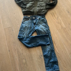Levi's jeans i blå denim - Snygga Levi's jeans i klassisk blå denim. De har en straight passform och är perfekta för en avslappnad stil. Jeansens design inkluderar de ikoniska fem fickorna och en knappgylf. Märkeslappen i läder sitter på baksidan av midjan.