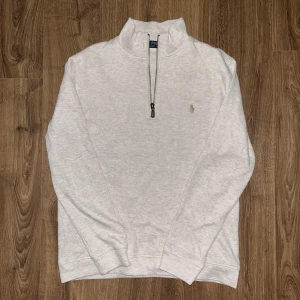 Tröja med dragkedja från Polo Ralph Lauren - Säljer en stilren tröja från Polo Ralph Lauren med halv dragkedja och broderad logga på bröstet. Perfekt för en avslappnad och snygg look. Tröjan har långa ärmar och är tillverkad i ett mjukt material.