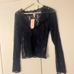 Marinblå spetsblus från Nelly - Elegant svart spetsblus från Nelly med långärmad design och v-ringad hals. Perfekt för en stilfull look med sitt genombrutna spetsmönster. Passar bra till både jeans och kjol.