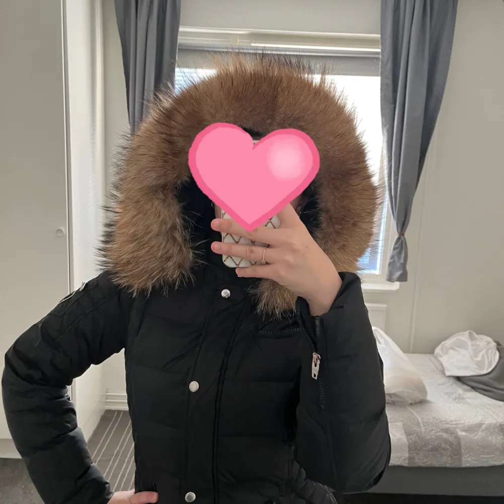 Snygg svart dunjacka från Rockandblue med en lyxig pälsdetalj på huvan. Jackan har dragkedja och knappar framtill samt en praktisk ficka med dragkedja på ärmen. Storlek M. ÄKTA PÄLS!!!. Takit.