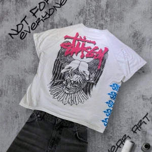 Vintage Stussy t-shirt  - Cool vit t-shirt från Stussy med ett stort grafiskt tryck på baksidan i svart och rosa. T-shirten har korta ärmar och ett unikt blått mönster längs ena sidan. Perfekt för dig som vill sticka ut. Storlek M, kvitto för äkthet finns 