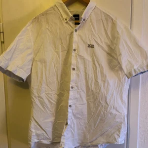 Vit kortärmad skjorta från Hugo Boss - Säljer en stilren vit kortärmad skjorta från Hugo Boss. Skjortan har en klassisk krage och knappar framtill. Perfekt för en avslappnad men ändå elegant look. Passformen är normal och materialet har stretch för extra komfort.