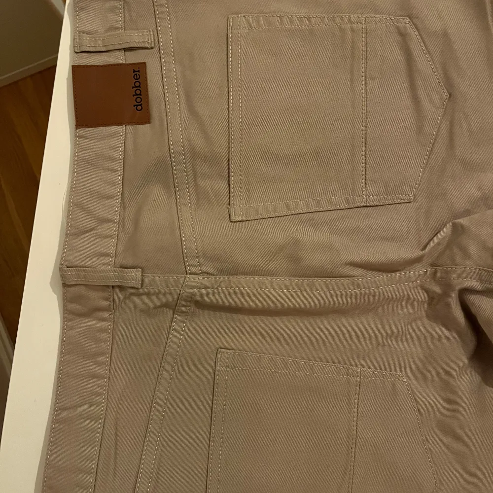 Snygga beige byxor från Dobber i storlek W32. De har en klassisk femficksdesign med knapp och dragkedja framtill. Perfekta för en stilren look.. Farkut & Housut.