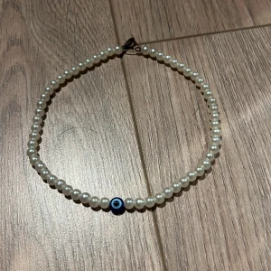 Pärlhalsband med blå detalj - Elegant pärlhalsband med vita pärlor och en unik blå detalj i mitten. Perfekt för att ge en stilren touch till din outfit. Halsbandet har en enkel låsning och passar de flesta tillfällen.
