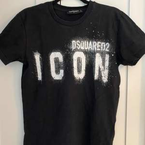 Säljer en svart t-shirt från Dsquared2 med texten 'ICON' i vitt på framsidan. Den är kortärmad och i bra skick. Perfekt för en casual look eller att styla upp för en fest. Passar både till jeans och shorts! Hör av er vid minsta fundering och pris kan diskuteras👑