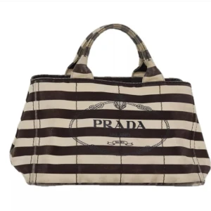 Prada Canapa väska - Denna väska är designad för att hjälpa dig varje dag. Väskan är praktisk att bära och moderiktig design.  Ursprung: Indien Material: canvas    Färg: brun Tillbehör: inga   Några tecken på användning, fläckar och trådar fransar, men överlag bra skick.
