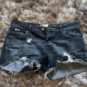 Mörkblå slitna jeansshorts - Säljer ett par mörkblå low waist jeansshorts från Denim. De har hål och fransiga kanter. Storleken är 38 men skulle säga att de passar 36 bra också.