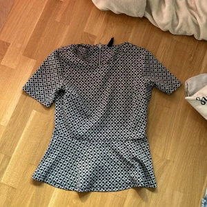 Mönstrad topp från Karl Edition - Säljer en snygg mönstrad topp från Karl Edition i storlek S. Toppen har ett coolt geometriskt mönster i svart och vitt och är kortärmad. Den har en dragkedja i ryggen för en stilren look. Perfekt för både vardag och fest!