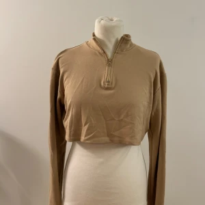 Beige croppad tröja från Romy - Säljer en snygg beige croppad tröja från nakd. Den har en dragkedja framtill och är långärmad, perfekt för en avslappnad stil. Tröjan är i storlek XS och passar perfekt till både vardag och fest. Superbekväm och lätt att matcha med andra plagg!