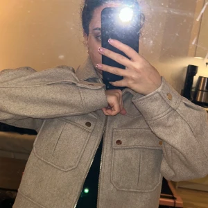 Beige jacka från Zara - Säljer en snygg beige jacka från Zara med dragkedja och knappar. Jackan har en croppad design och två stora fickor framtill. Perfekt för en stilren look!