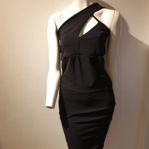 Svart oneshoulder klänning från PrettyLittleThing - Snygg svart oneshoulder klänning från PrettyLittleThing. Den har en tight passform och en elegant slits baktill. Perfekt för en kväll ute eller en speciell tillställning. Klänningen är tillverkad i ett mjukt och stretchigt material för bästa komfort.