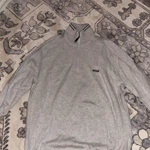 Grå tröja med dragkedja från BOSS - Säljer en  grå tröja från BOSS med halv dragkedja och hög krage. 