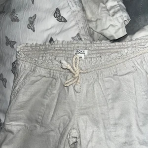 Beige linnebyxor från Roxy - Säljer ett par bekväma beige byxor från Roxy. De har en elastisk midja med snörning och raka ben. Perfekta för en avslappnad stil. Säljer dom pga att dom aldrig kommer till användning! Inte tvättade någon gång alltså helt nya! 