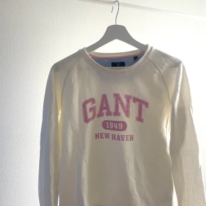 Vit långärmad tröja från GANT - Säljer en vit långärmad tröja från GANT med rosa tryck framtill. Tröjan har en rund halsringning och är perfekt för en avslappnad stil. Den är gjord i ett mjukt bomullsmaterial som känns skönt mot huden. Använd fåtal gånger, som ny! Tunnare material.