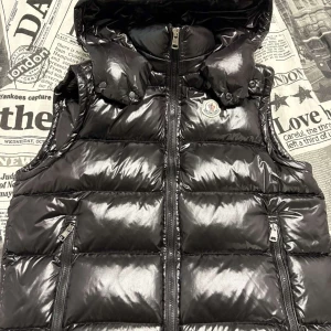 Svart dunväst från Moncler - Snygg svart dunväst från Moncler med glansig yta, västen är i storlek 2 vilket motsvarar storlek M, västen är i perfekt skick, vid frågor hör av er ! 