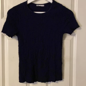 Mörkblå topp från Zara - Snygg mörkblå topp från Zara med korta ärmar. Perfekt för en stilren look. Toppen har en rund halsringning och är tillverkad i ett stretchigt material för en bekväm passform.