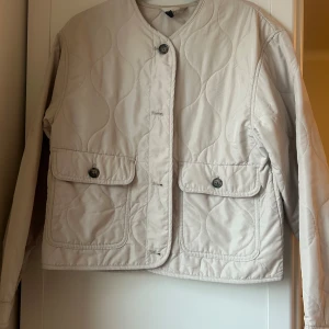 Beige quiltad jacka - Säljer en stilren beige quiltad jacka från C&A. Jackan har långa ärmar och knappar framtill. Den har två praktiska fickor med knappar. Perfekt för en avslappnad look.