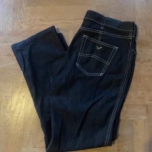 Svarta jeans från Armani Jeans - Snygga svarta jeans från Armani Jeans med kontrasterande vita sömmar. Klassisk femficksdesign och en diskret logga på bakfickan. Perfekta för en stilren look.