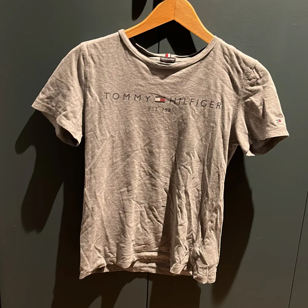 Säljer en grå t-shirt från Tommy Hilfiger i ekologisk bomull. T-shirten har korta ärmar och ett tryck med märkesloggan på framsidan. Lite nöt tryck men ändå väldigt bra skick. T-paidat.