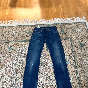 Levis 501 jeans i blå denim - Säljer ett par klassiska Levis 501 jeans i blå denim. De har en straight passform och är lågmidjade. Perfekta för en avslappnad stil med slitna detaljer som ger en vintagekänsla.  W27 L30. Nypris 1099