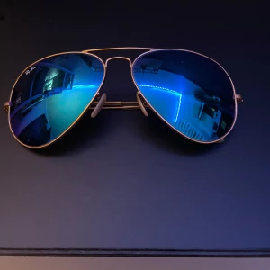 Blå pilotglasögon från Ray-Ban - Snygga pilotglasögon från Ray-Ban med blå lins och tunn guldfärgad metallram/båge. Perfekta för en stilren look. De har justerbara nässadlar för extra komfort. Köpta för 1250kr på Synsam. Mitt pris: 399kr!