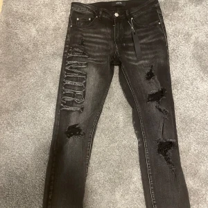 Amiri - Snygga svarta jeansbyxor från Amiri med slitna detaljer och broderad text längs benet. Byxorna har en slim passform och är tillverkade i denim storleken är 30 vilket motsvarar S