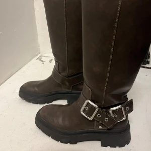 Bruna stövlar med spänne - Snygga bruna stövlar i skinn med robust sula och dekorativa spännen. Perfekta för en stilren look med en touch av edge. Köpta från Zara för 800kr 
