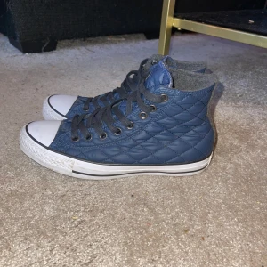 Blå quiltade sneakers från Converse - Snygga blå quiltade sneakers från Converse med klassisk vit tå och svart snörning. Skorna har en hög modell med det ikoniska Converse-märket på sidan. Perfekta för en stilren look. Nypris:470