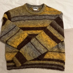 Randig tröja från Weekday - Säljer en mysig randig tröja från Weekday i jordnära färger. Tröjan har en kombination av bruna, gula och gråa ränder och är perfekt för kyligare dagar. Den har långa ärmar och en rund halsringning.