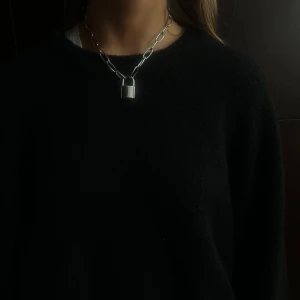009 - Snyggt halsband med ett stort hänglås som hänge. Kedjan är i en chunky stil och ger en modern och edgy look. Perfekt för att ge din outfit en unik touch.